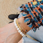 white pearl stretchy bracelet on the wrist with other gold bracelets