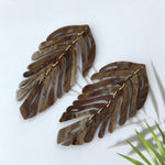 Pair of wooden leaf-shaped earrings on a white background with a green plant leaf.