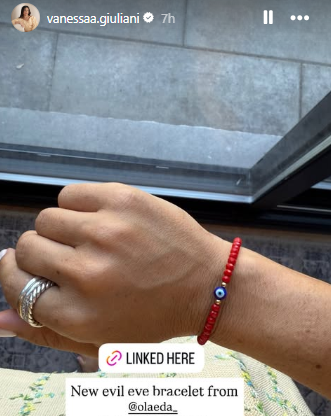 Hand wearing a red bracelet with a blue bead, silver ring, and silver chain, with text overlay on an Instagram post.