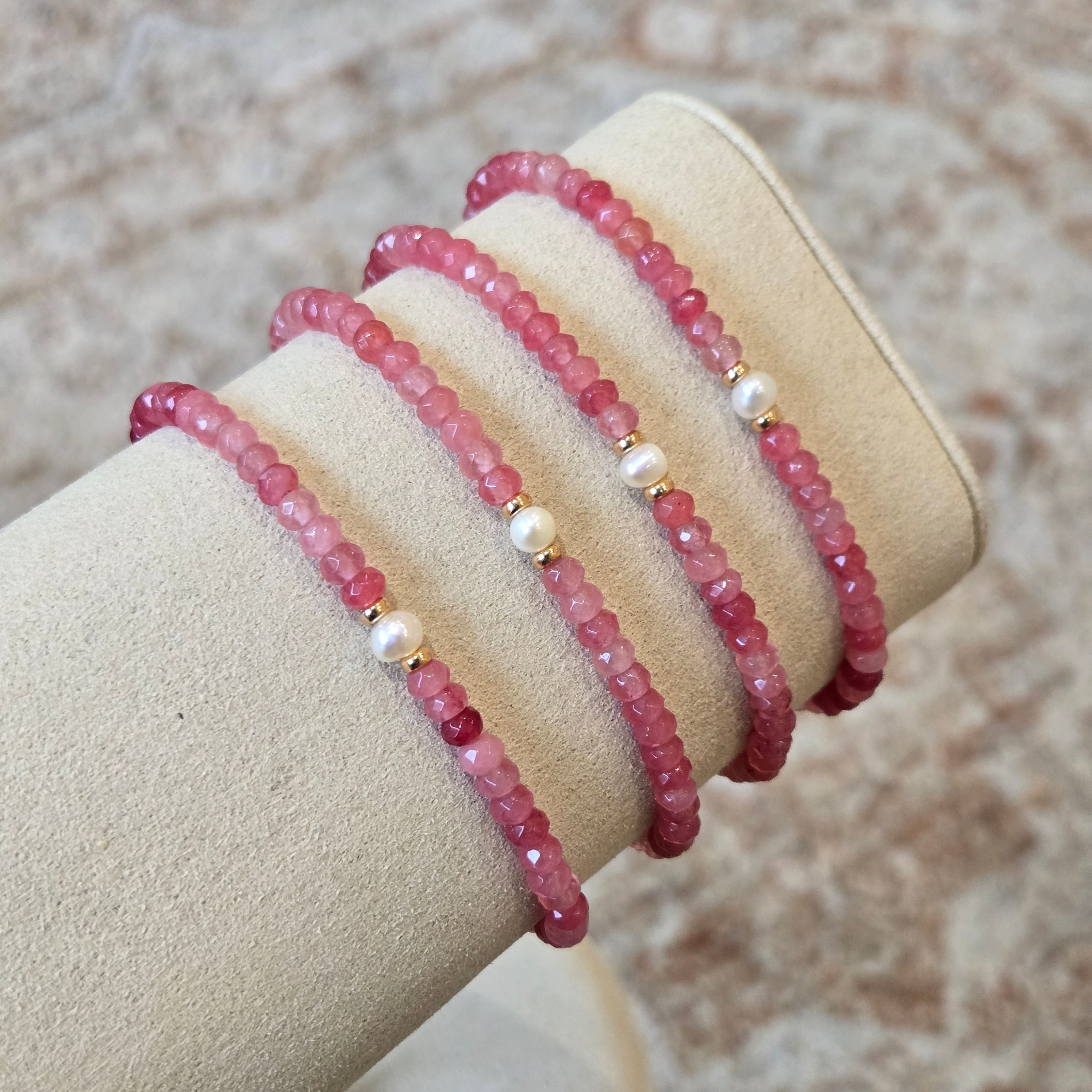 Three pink beaded bracelets on a beige stand with a neutral background