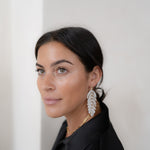 Woman wearing large feather earrings against a plain background