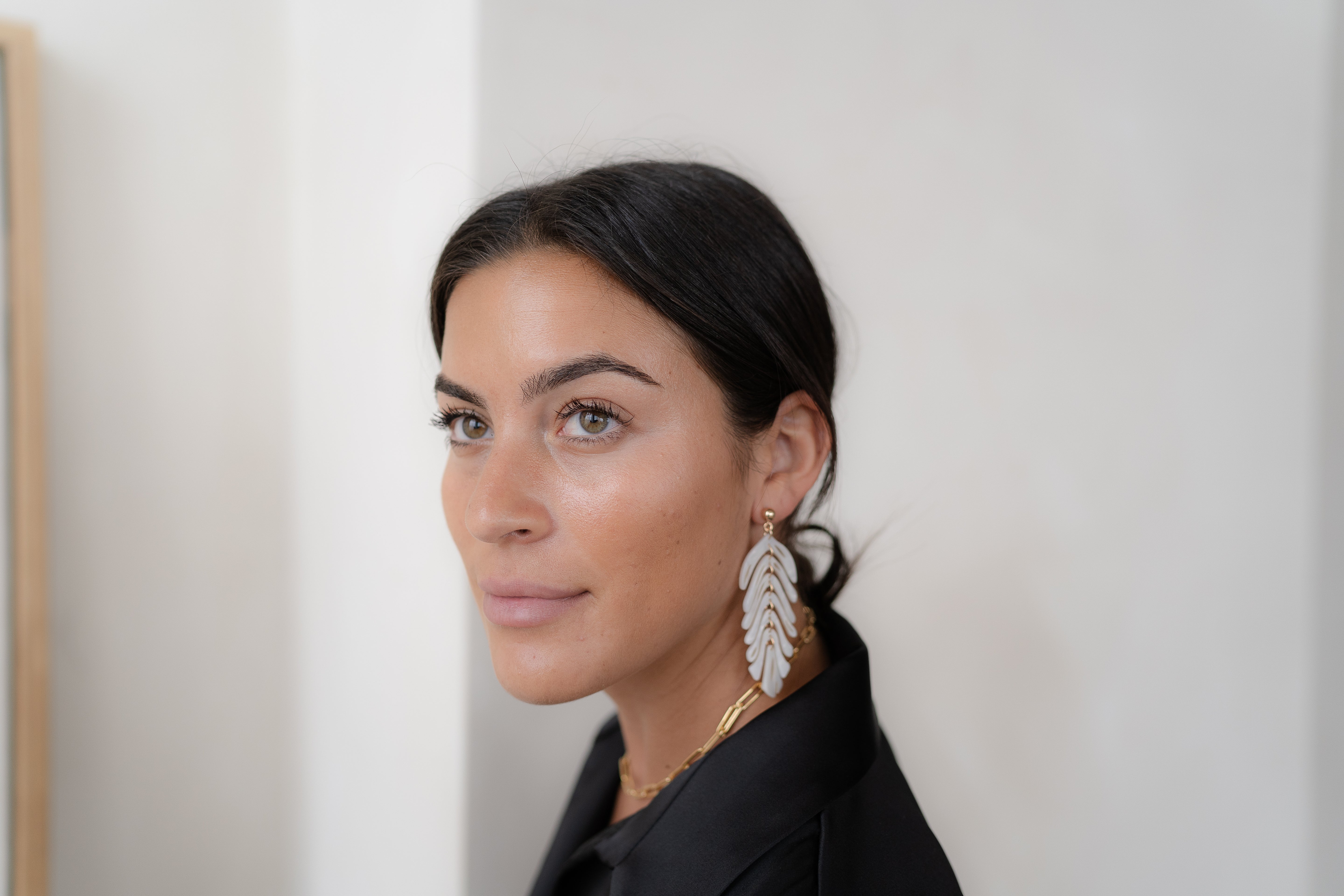 Woman wearing large feather earrings against a plain background