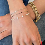 Close-up of a hand wearing gold bracelets and a ring on a denim surface.