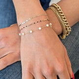 Close-up of a hand wearing gold bracelets and a ring on a denim surface.