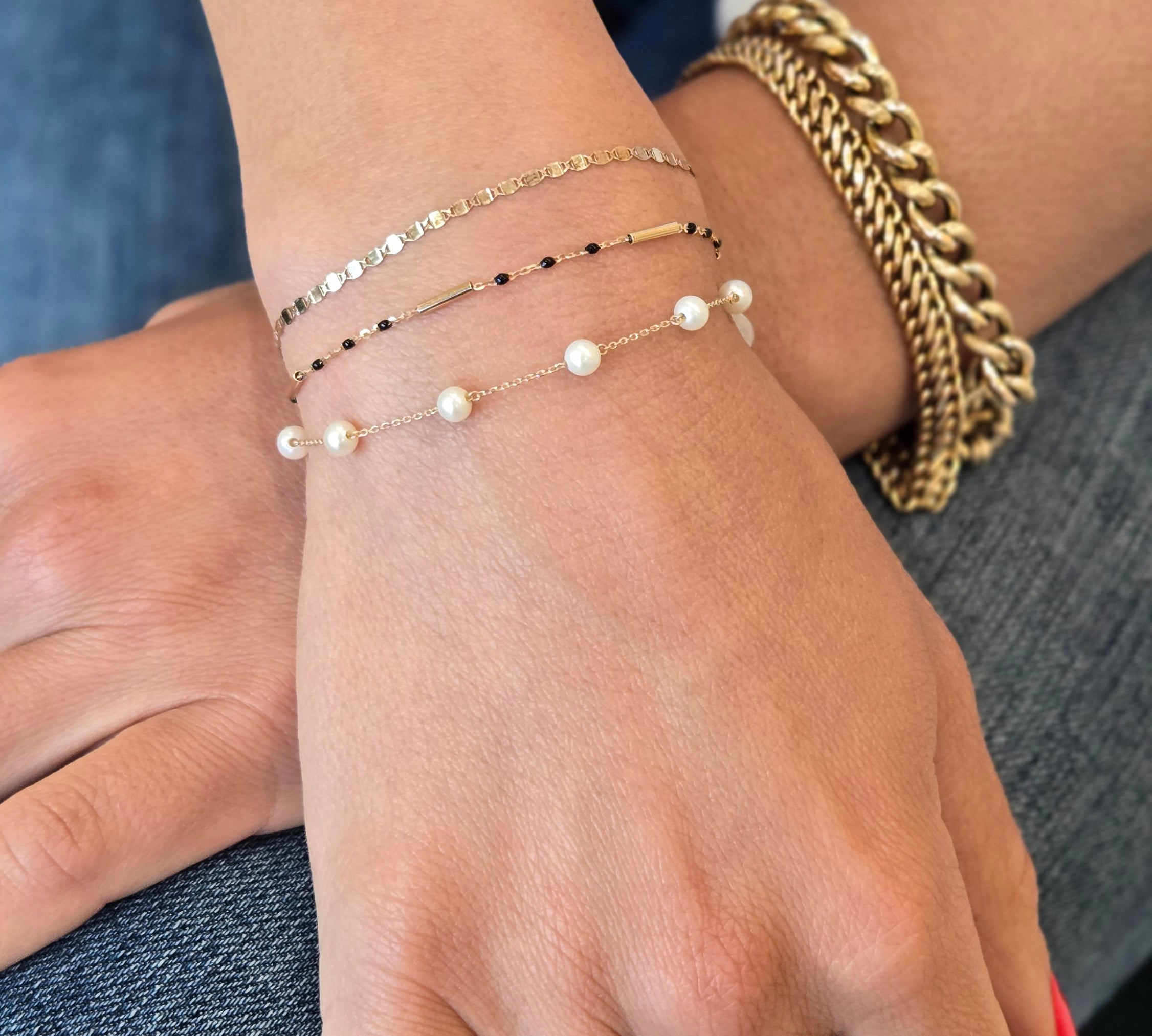 Close-up of a hand wearing gold bracelets and a ring on a denim surface.