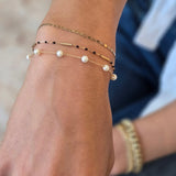 Close-up of a wrist wearing multiple gold bracelets with beads on a blurred background