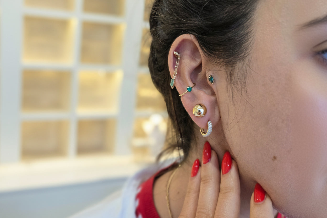 Close-up of a person's ear with multiple earrings, wearing a red top.