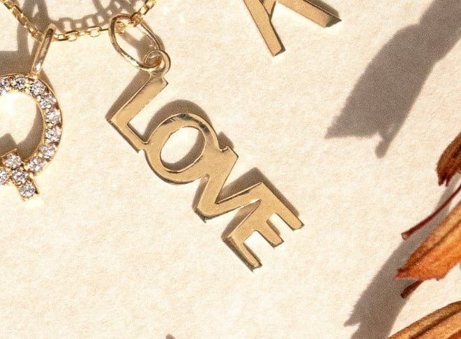 Gold letter charms on a beige background with dried grass