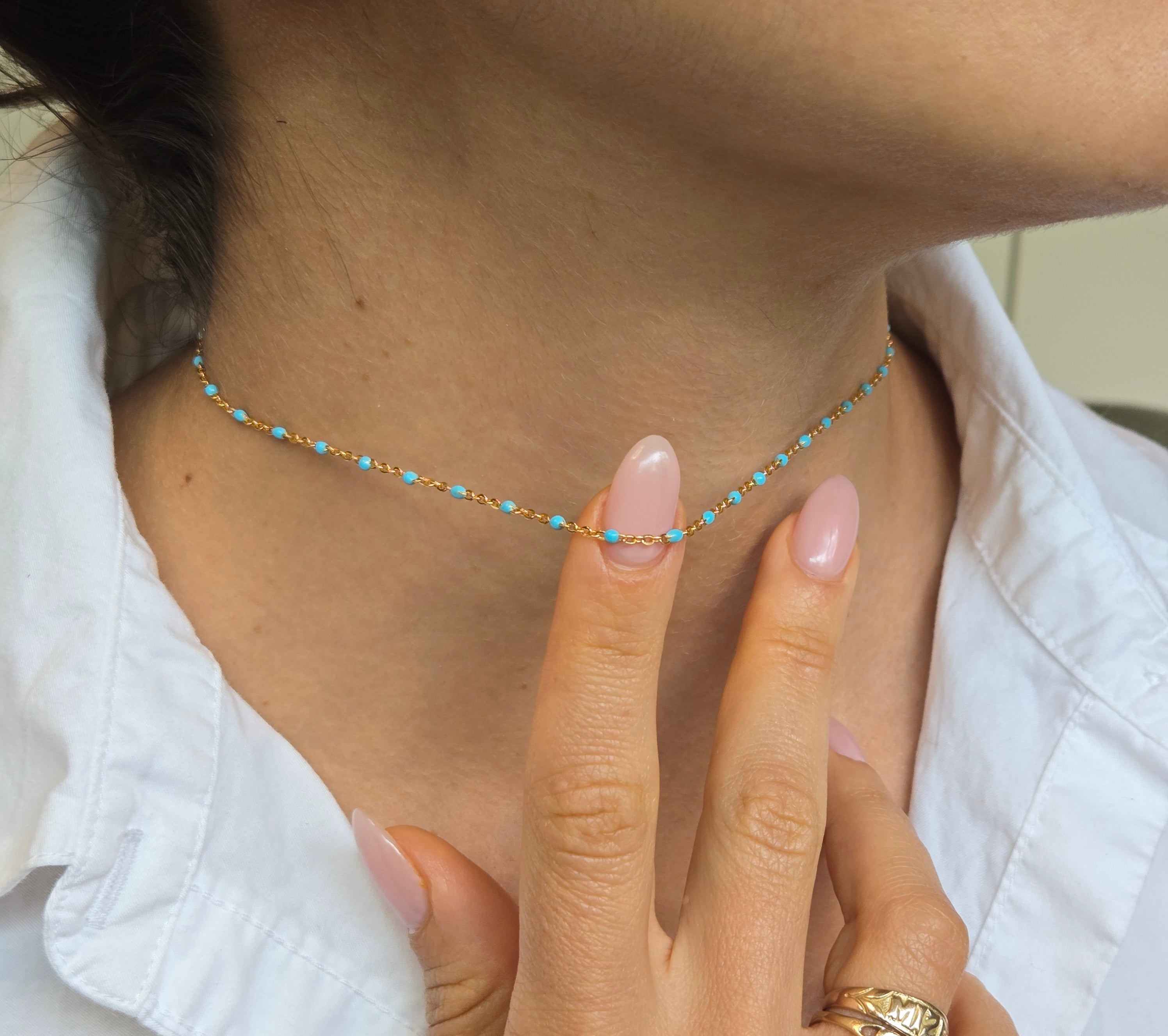 Close-up of a hand wearing a gold ring with a turquoise beaded necklace on a white shirt background