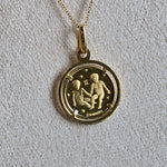 Gold necklace with a round pendant featuring an astrological symbol on a light gray background