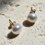 Pair of pearl earrings on a textured beige surface