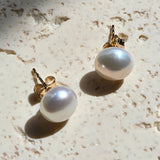Pair of pearl earrings on a textured beige surface