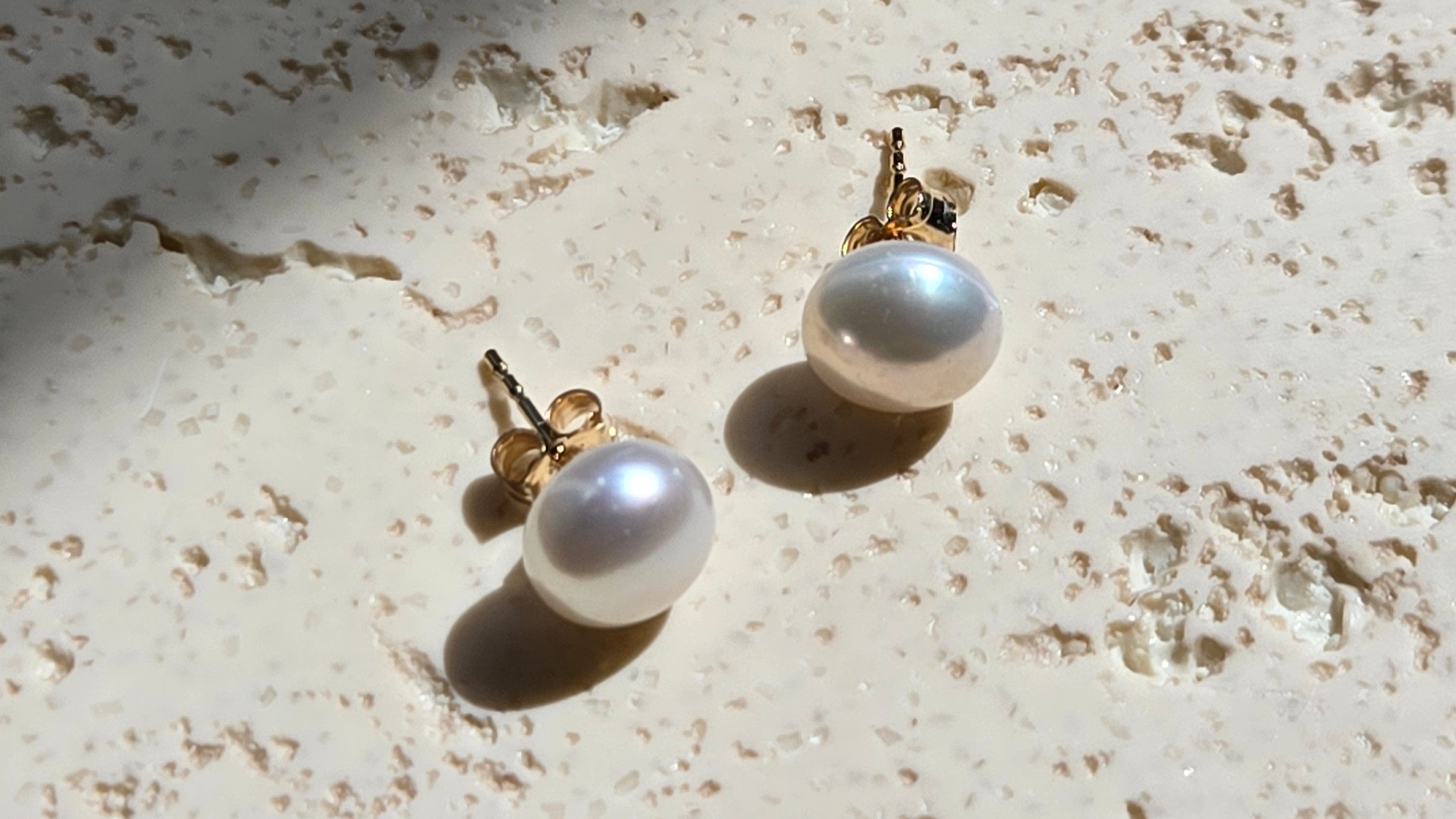 Pair of pearl earrings on a textured beige surface