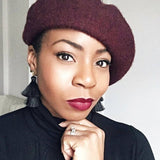Woman wearing a maroon beret with tassel earrings and dark lipstick.