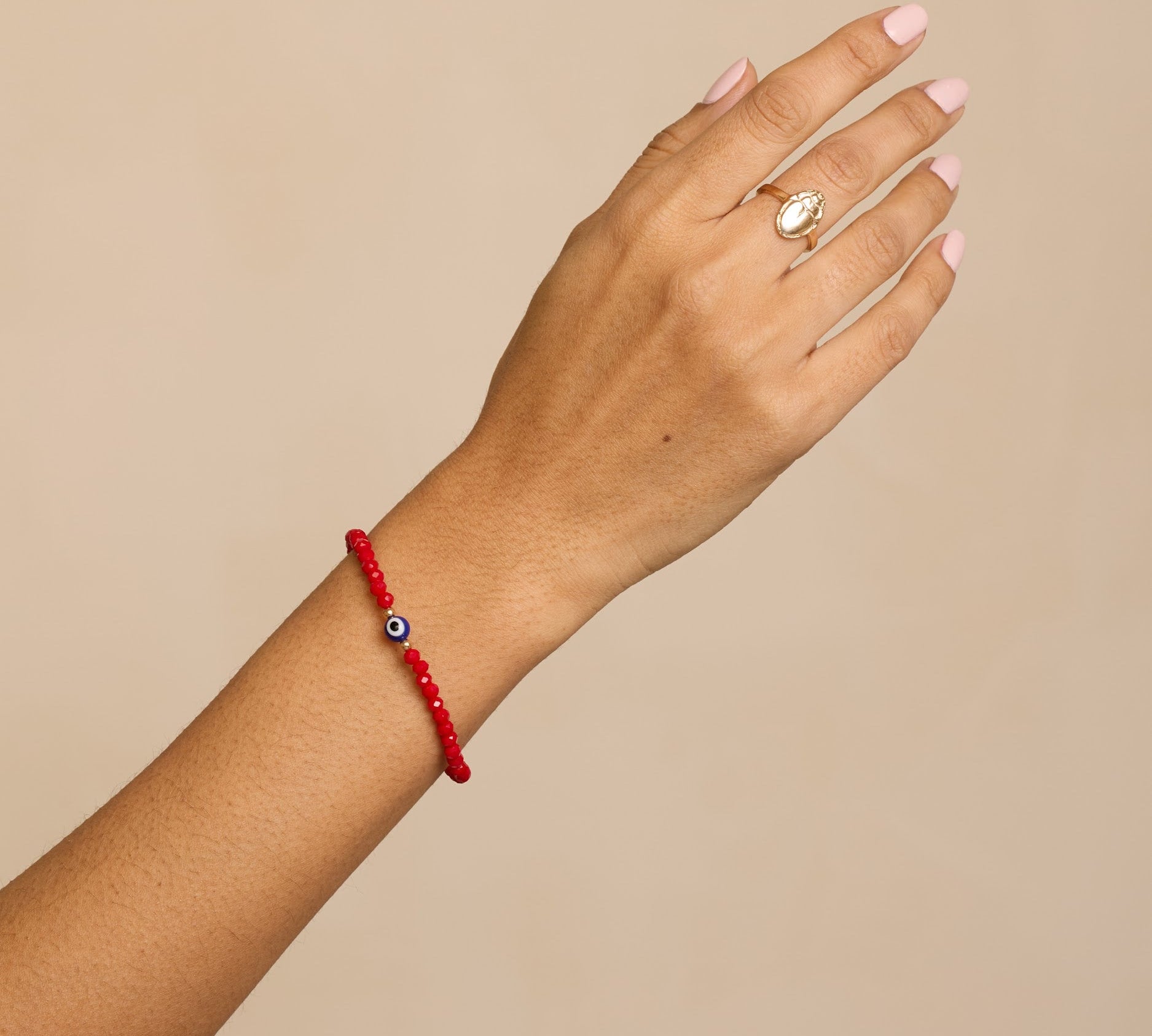 Hand wearing a red bracelet with a beige background