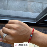 Hand wearing a red bracelet with a blue bead, silver ring, and silver chain, with text overlay on an Instagram post.